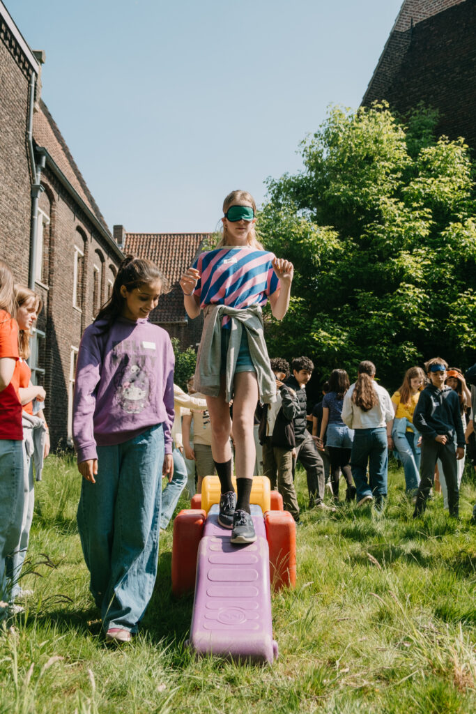 Stagiair helpt geblinddoekte TAJO-jongere over een parcours.